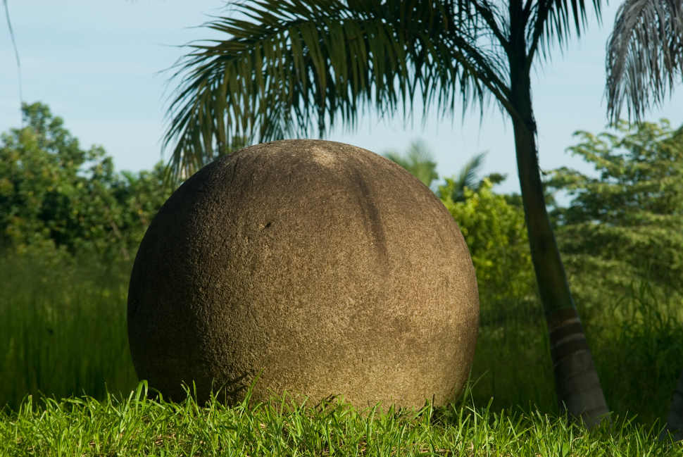 Esfera de piedra precolombina del Diquís sobre el césped, junto a una palmera